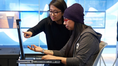 Due persone che guardano lo schermo di un portatile e conversano.