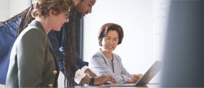 Tre persone che indossano abiti da ufficio collaborano intorno a un portatile in un ufficio.